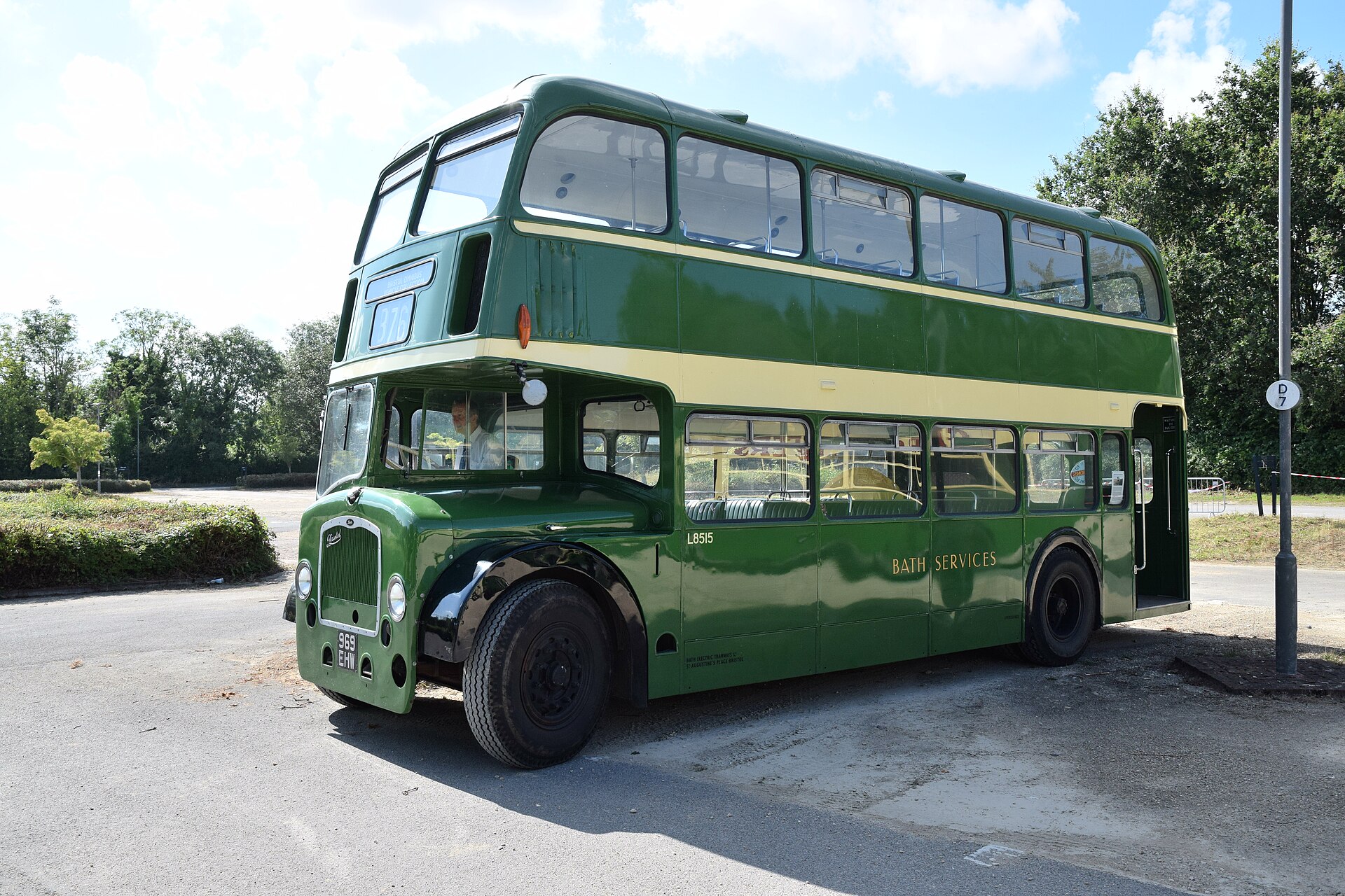 Green and cream Bristol Lodekka double-decker bus in bright sunshine, driver seated in the half-cab, photographed from the front three-quarter