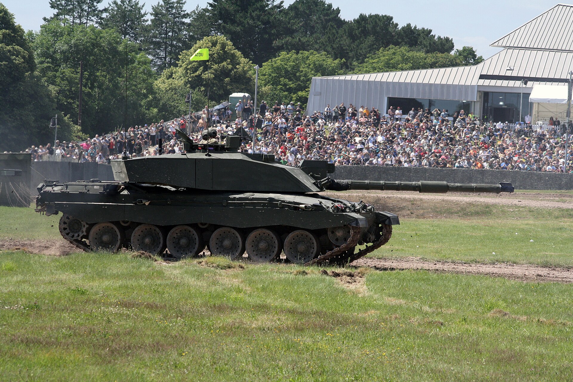 A Challenger 2 tank crosses the Bovington arena with thousands of spectators filling the banked grandstand behind it