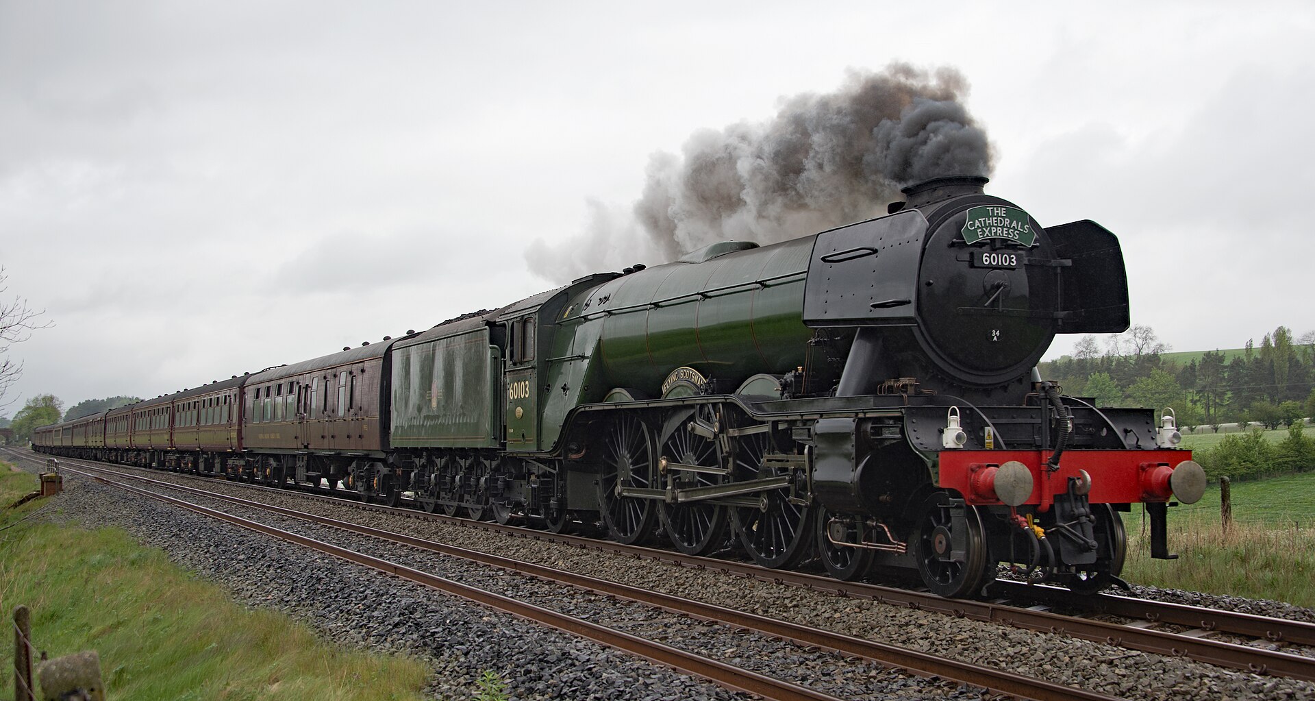 Flying Scotsman works a mainline charter at speed, throwing dense plumes of white steam into the sky above open Cumbrian countryside.