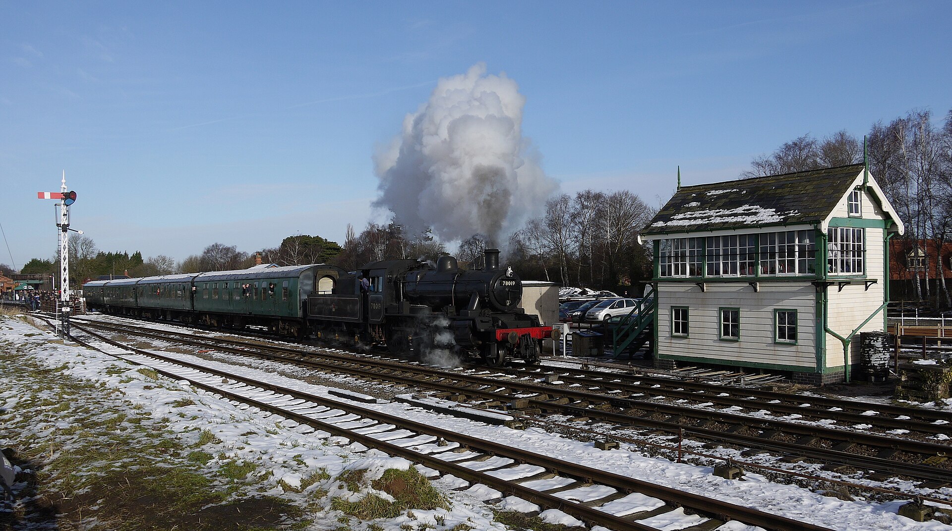 A steam locomotive stands in snow at Quorn and Woodhouse station during a Great Central Railway winter gala, steam and snowfall merging in the cold air.