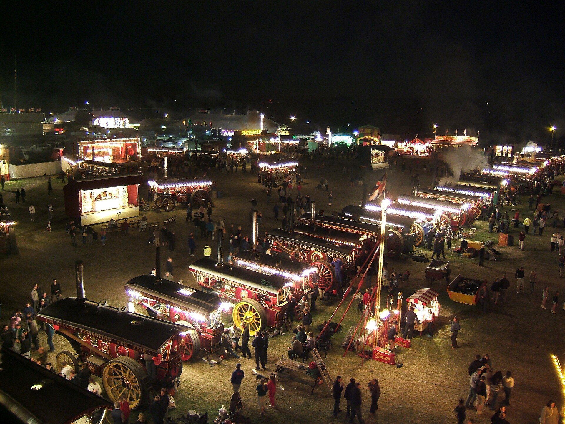 A line-up of showman's engines glowing with strings of lights in the fairground at night at the Great Dorset Steam Fair, photographed from the big wheel in 2007.